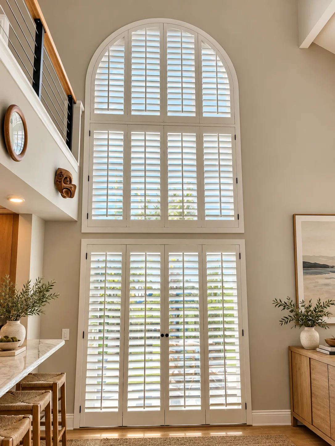White arched plantation shutters on a two-story window wall above French doors in a great room