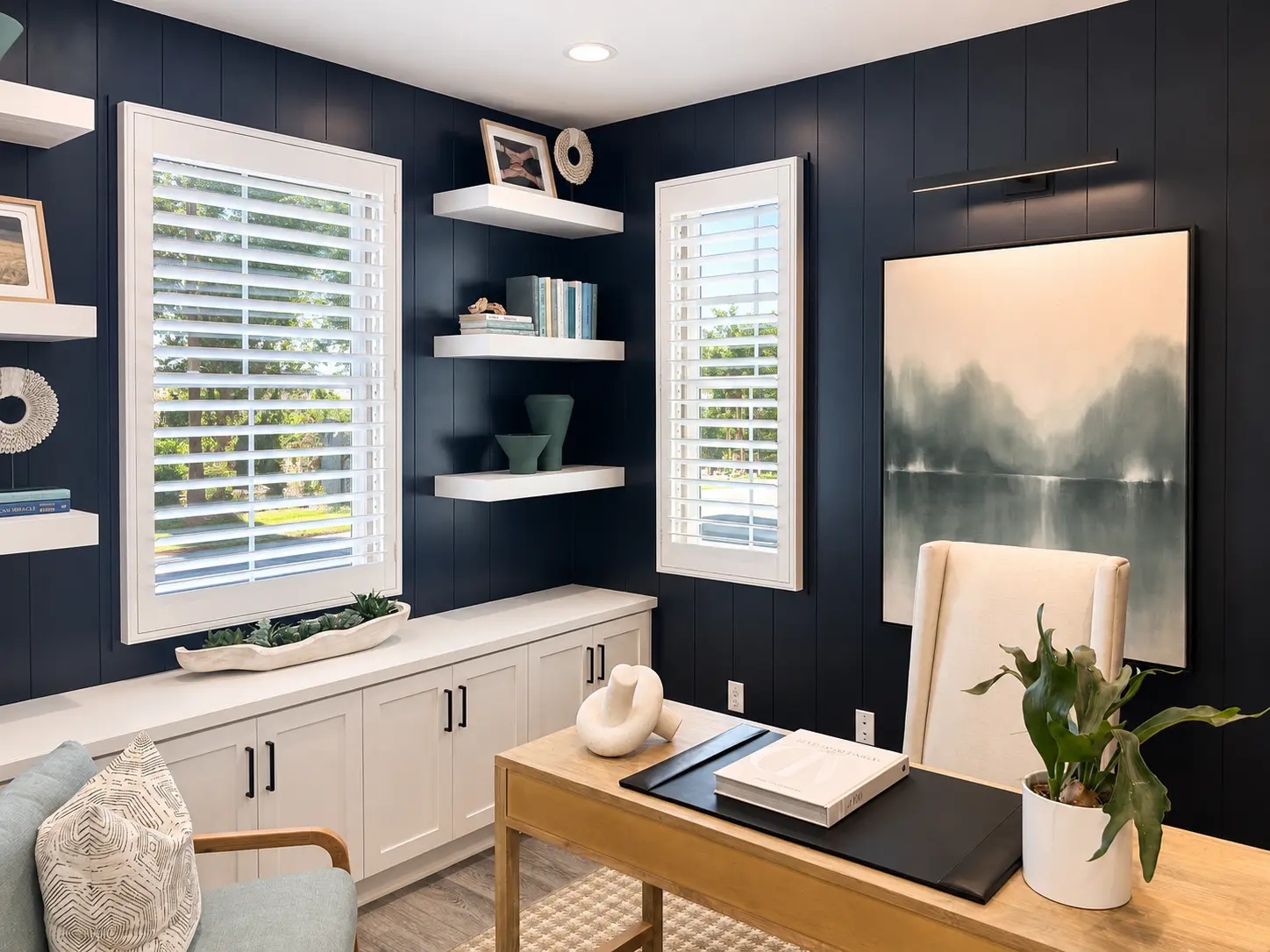 Wide-louver designer plantation shutters on tall windows in a navy-walled home office