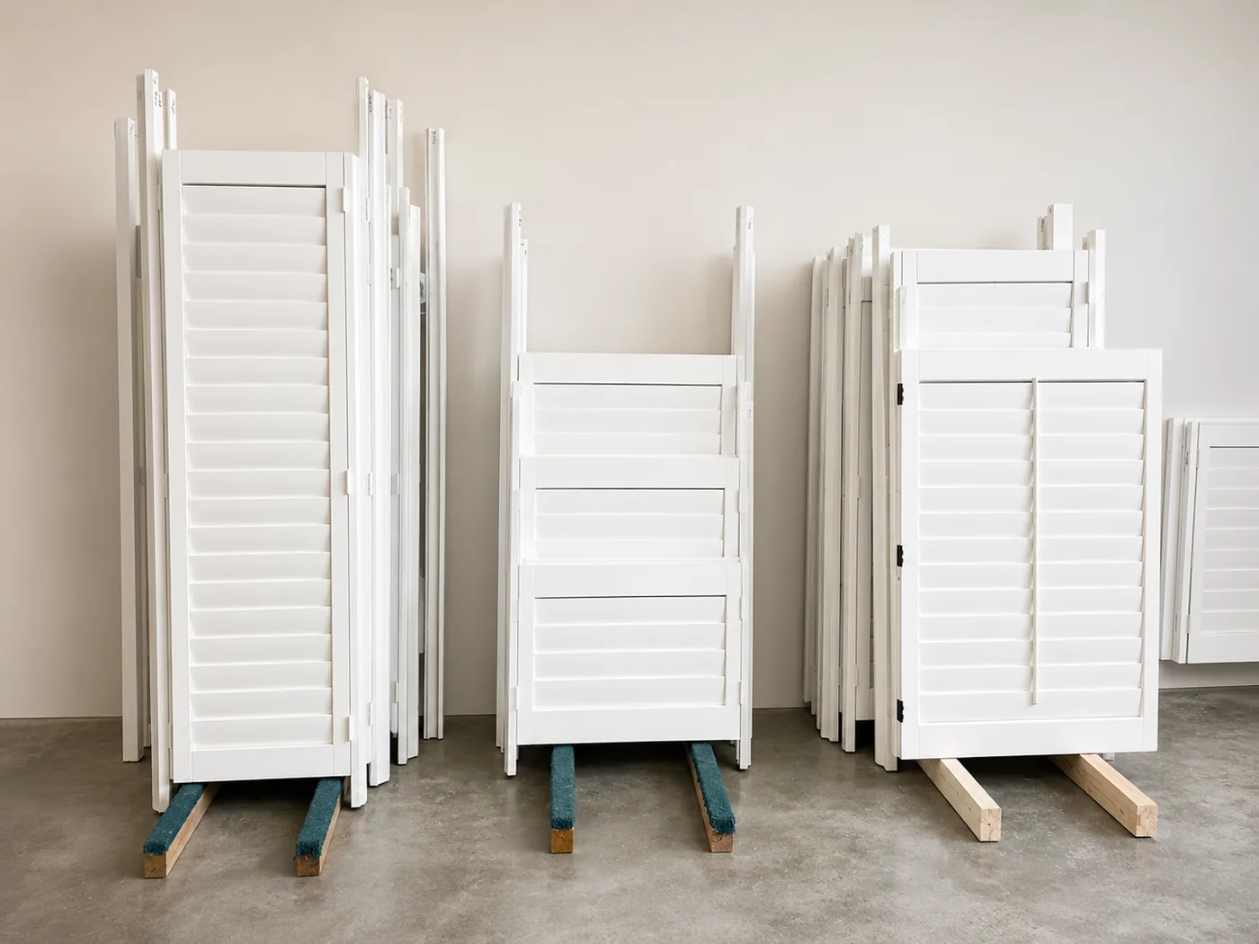 Rows of finished white plantation shutter panels staged upright on wood rails on the floor of Golden West's Lake Forest factory, waiting to be installed