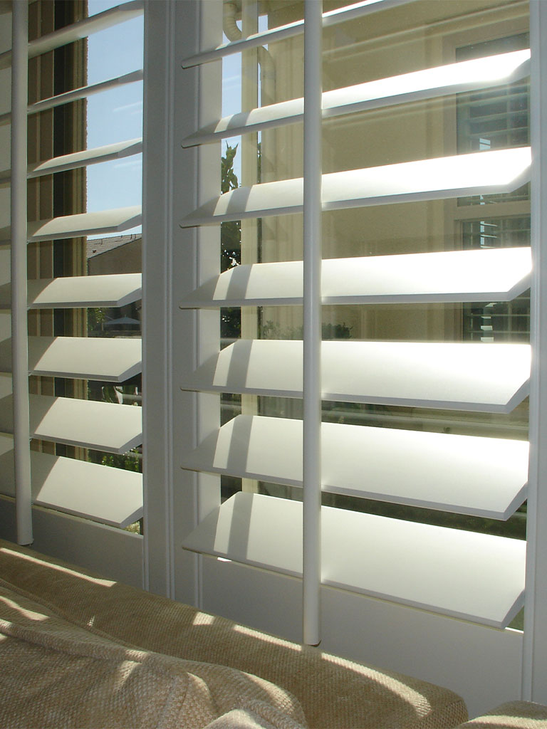 White plantation shutters in a sunny Orange County home interior, showcasing energy efficiency and privacy